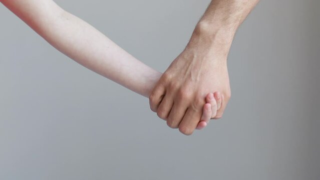 Man and child join hands and hold against the background of a white wall