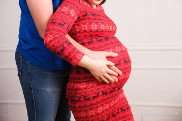 Husband hugs pregnant wife and pats on the belly, pregnancy for Christmas, close-up, copy space