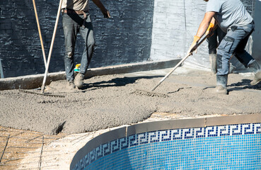 Workers distributing the concrete with rakes around the pool, fixing the garden