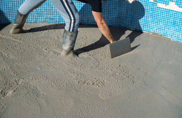 Worker spreading and smoothing the concrete with a manual shovel