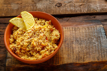 Couscous masfouf with dried fruits and nuts in a clay plate on a wooden board on the table.
