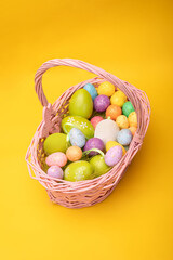 Easter basket full of colorful Easter eggs, on a yellow background. Easter holiday concept, photo with a copy space.
