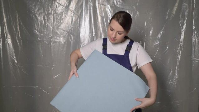 Woman builder in blue overalls with roll of blue wallpaper.