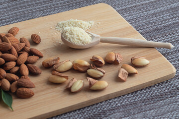 Close-up of almond flour in a wooden spoon, almond kernels, peeled and not, on a wooden board on a napkin.