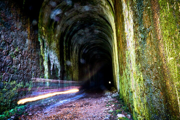 Tunel de ferrocarril antiguo con musgo en las paredes y las luces de un auto cruzando terraplen...