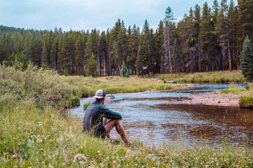 Man sitting on edge of stream looking into the woods