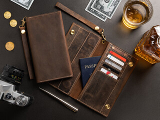 Concept of flatlay business accessories. A purse made of craft textured brown leather with compartments for credit cards, dollar bills with coins and a glass of whiskey on a grainy gray background.