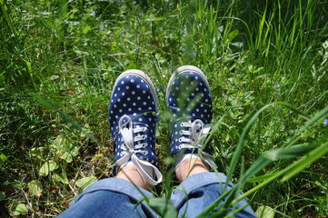 sneakers on girl legs on grass during sunny summer day.Female feet in gumshoes on green grass background