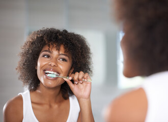 Keeping her smile. Shot of a a young woman brushing her teeth.