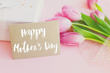 Obraz premium Happy mothers day text on greeting card, pink tulips bouquet and gift box on pink background. Stylish greeting card. Happy Mother's Day, gratitude and love to mom. Handwritten lettering