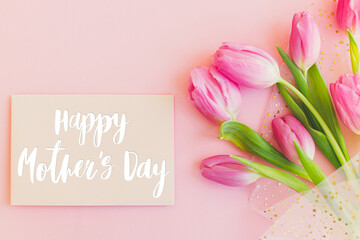 Happy mothers day text on greeting card and pink tulips on pink background. Stylish greeting card. Happy Mother's Day, gratitude and love to mom. Handwritten lettering