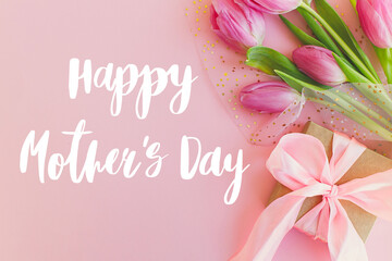 Happy mothers day text on pink tulips bouquet and gift box on pink background. Stylish greeting card. Happy Mother's Day, gratitude and love to mom. Handwritten lettering