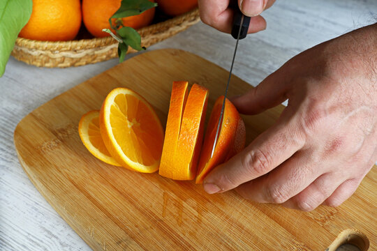 a man slicing an orange on a wooden chopping board
