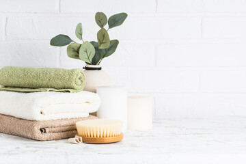 Spa background in white spa salon or bathroom. Stack of towels, shampoo bottle, candles and vase with plant.