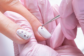 Manicurist drawing on female nails. Woman in nail salon receiving manicure by beautician. Manicure...
