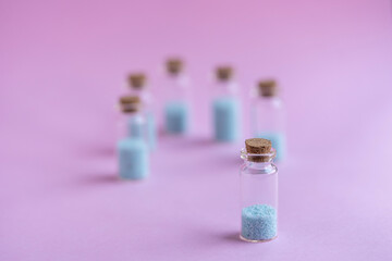 6 botellitas de cristal con tapa de corcho con relleno de piedritas color turquesa y fondo liso de color rosado  y desenfoque del fondo