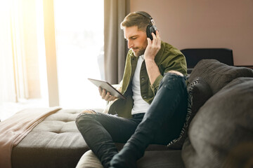 Handsome guy wearing headphones enjoys music sit on the comfortable sofa when using a computer tablet