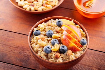 Tasty oatmeal with berries, nuts and apples on wooden table. Bowl of oatmeal porridge with blueberries and honey. Healthy breakfast. Top view