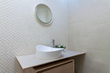 Naklejka na ściany i meble White washbasin with faucet on wooden countertop in minimalist modern bathroom. Scandinavian interior with tiled mosaic wall wall and round mirror. Copy space and nobody.