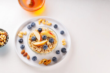 Oatmeal with berries, nuts and honey on a white background. Oatmeal porridge with blueberries and sliced apple in bowl. Healthy breakfast. Top view. Copy space