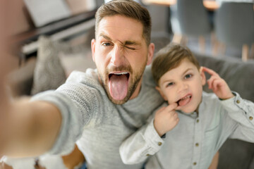 Father and son spending time together on sofa taking selfies and making grimaces