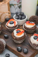 Chocolate muffin cupcakes. Cream cheese, a blueberry and sliced strawberry. Selective focus shot.