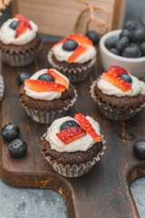 Chocolate muffin cupcakes. Cream cheese, a blueberry and sliced strawberry. Selective focus shot.