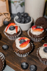 Chocolate muffin cupcakes. Cream cheese, a blueberry and sliced strawberry. Selective focus shot.