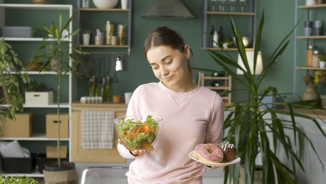A Woman in the Kitchen Chooses Between Healthy Organic Food and Glazed Donuts.