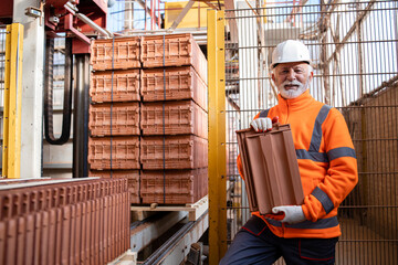 Production of roof tiles or shingle for construction industry. Factory worker holding tiles in manufacturing production hall.