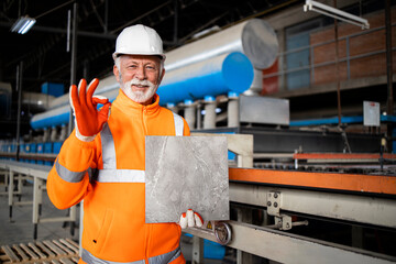 Successful ceramic tile production and factory worker holding the product.