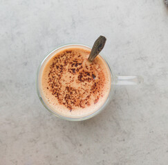 A glass cup with double wall of coffee. The hot drink with spoon in a transparent mug, on a gray background, isolated. Hot chocolate with light foam and cocoa powder, top view.