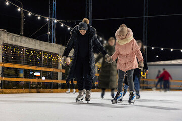 mother and daughter skate on the ice rink in the evening