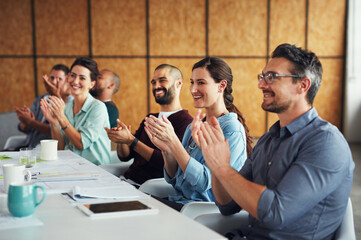 The creative process. Shot of a group of colleagues clapping together at a table in an office.