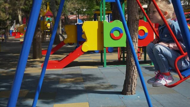 Little blond girl having fun on a swing outdoor. Summer playground