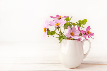 Fresh delicate pink flowers in white jar on rustic white wooden background.