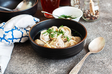Russian treditional pelmeni with bouillon in a black bowl on a gray background.