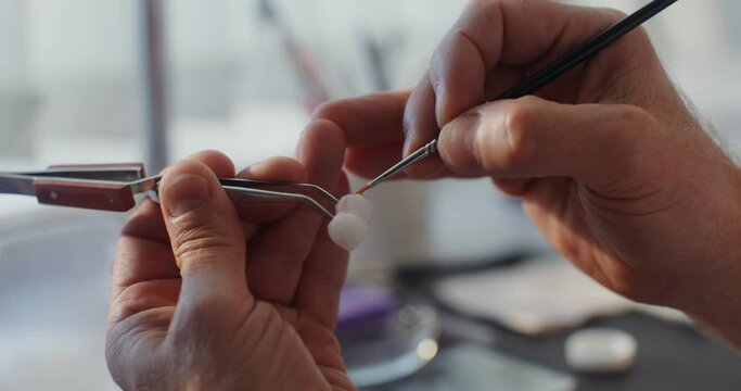 Close-up of painting a ceramic dental crown with a thin brush by hand