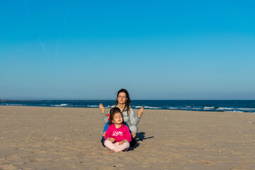 chica , niño y niña pequeña haciendo yoga. en postura mariposa  , en una playa de arena...