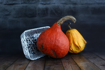 Multi-colored decorative pumpkins and a ceramic plate on a table against a dark brick wall.