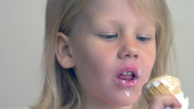 Little girl in a pink dress eating ice cream in a cone on a white background