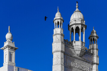 Fototapeta premium Bird flying above white mosque towers against a blue sky in Mumbai