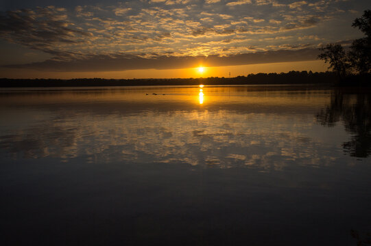 The sun rises below a cloud front, reflected in the waters of Mosquito Creek Lake in Ohio
