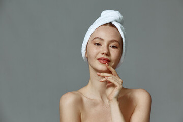 Beautiful young girl with towel on head, clean healthy skin after skincare treatment on gray studio background