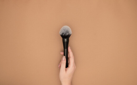 Professional make-up powder brush cosmetic in female beautician's  hand isolated on beige background