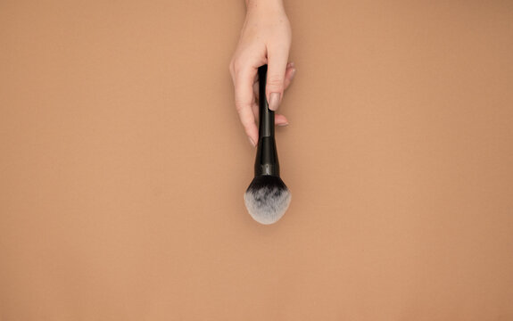 Professional make-up powder brush cosmetic in female beautician's  hand isolated on beige background