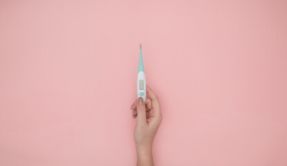 woman hand holding white thermometer on pink background. Isolated thermometer.