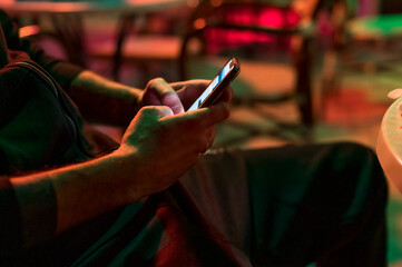 Man texting on the phone in the club sitting on chair.