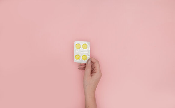 Woman holding blister with cough drops pills tablets on pink background, top view. Space for text
