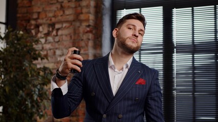 A handsome attractive man in an expensive suit sprinkles perfume on himself